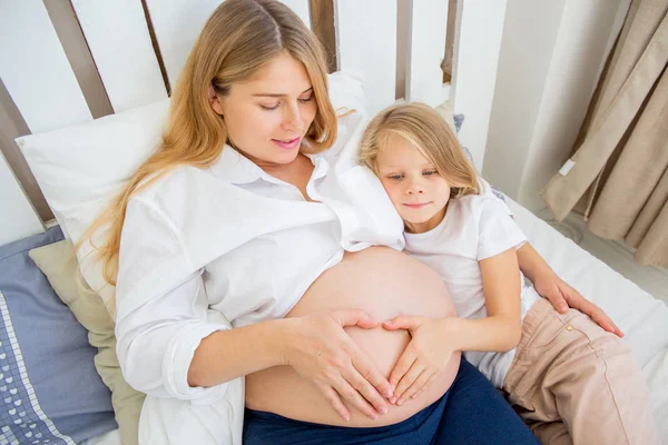 Glücklich lächelnde schwangere Mutter umarmt ihre Tochter zu Hause — Stockfoto