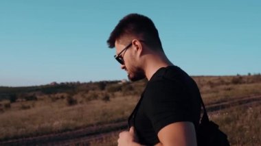 Tarlanın ortasında yürüyen genç bir adamın portresi. Sırt çantalı aktif erkek turist doğal alanda yürüyor..