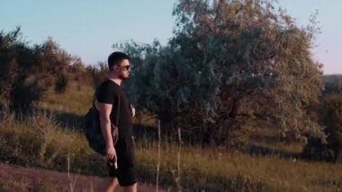 Genç bir ormanın ortasında, kır yolunda siyah tişört giymiş bir erkek turistin 4K videosu. Yandan çekilen genel çerçeve