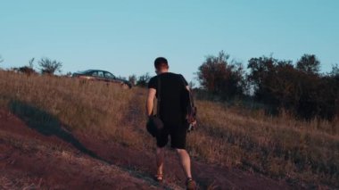 Doğada bir yolculuktan sonra aktif bir turist arabaya geri döner. Genç adam tişört ve siyah şort giyiyor ve aksesuar olarak bir retro kamerası var..