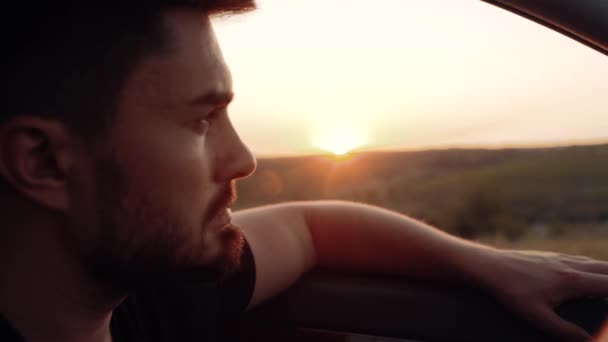 Close-up de um jovem europeu dirigindo um carro ao pôr-do-sol. Homem sério assistindo o pôr do sol da roda do carro que ele está dirigindo — Vídeo de Stock