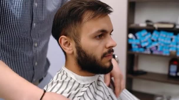Barberaren förbereder klienten för en klippning. Modernt koncept för småföretag. Den karismatiske unge mannen är glad och redo för en ny frisyr. — Stockvideo