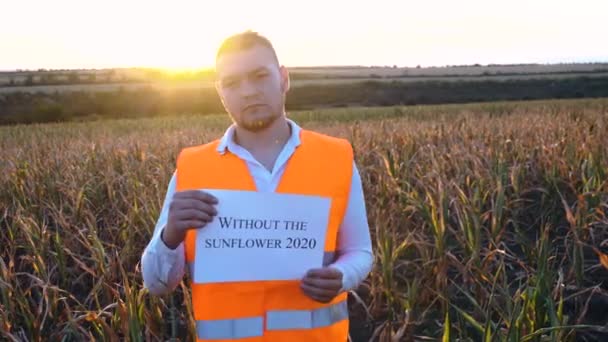 Porträtt av en sorgsen ung bonde som innehar en plakett med texten No sunflower in 2020. — Stockvideo