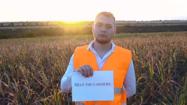 Porträtt av en sorgsen ung bonde som håller en plakett med inskriptionen Hjälp bönderna. — Stockvideo