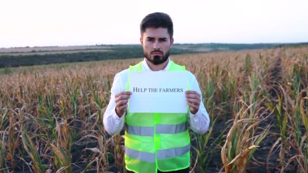 Портрет депрессивного молодого фермера с плакатом в руке с сообщением ПОМОГИТЕ этим фермерам. — стоковое видео