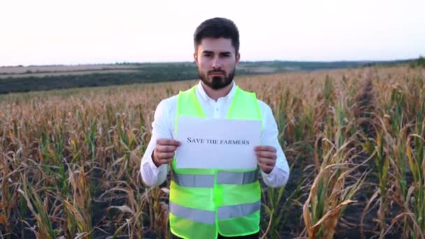 Porträtt av en ung deprimerad bonde med ett plakat i handen med budskapet Rädda bönderna. — Stockvideo