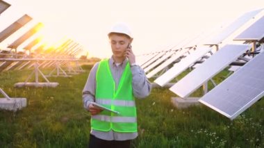 Elinde klasör olan genç bir mühendis yürürken telefonla konuşuyor..