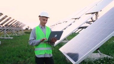 Genç mühendis güneş panellerinin yanında dizüstü bilgisayarını kullanıyor. Sonunda gururla gülümsüyor..