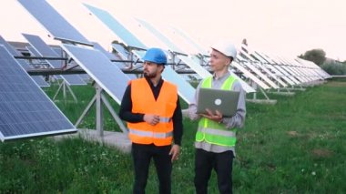 Güneş çiftliğinde dizüstü bilgisayarı olan iki mühendis, özel bir üniformanın içinde duruyorlar..
