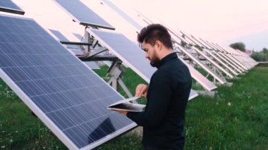 Başarılı bir yatırımcının portresi elinde dizüstü bilgisayarla güneş panelleri olan bir alanın önünde..