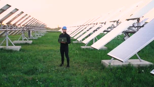 Dizüstü bilgisayarla çalışan mühendis güneş pillerinin yanında duruyor.. — Stok video