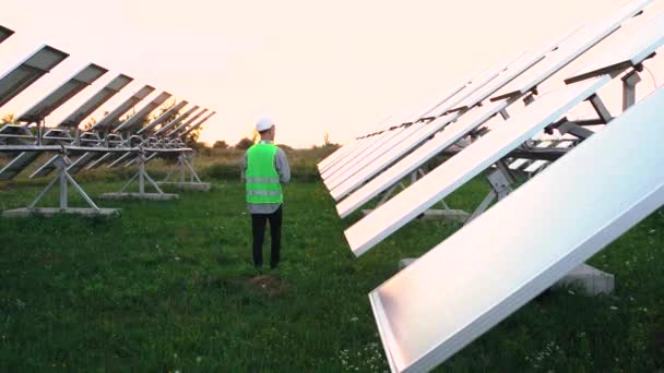 Правильно оборудованный кавказский инженер проверяет солнечные панели и отмечает результаты на ноутбуке. — стоковое видео