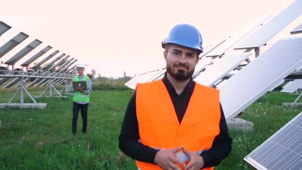 Ingeniero de casco protector que camina en el campo del panel solar y mira directamente a la habitación. — Vídeos de Stock