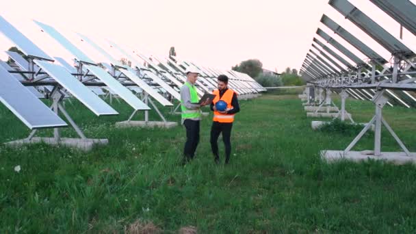 Twee jonge Kaukasische ingenieurs leren hoe ze een laptopplan voor zonnepanelen in de buitenlucht kunnen bouwen. — Stockvideo