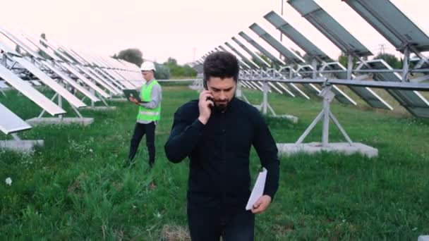Бізнесмен під час розмови по телефону біля будівництва сонячних батарей . — стокове відео