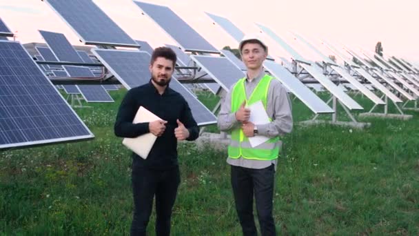 Porträtt av två glada ingenjörer mot bakgrund av solpaneler. — Stockvideo