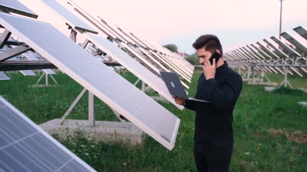 Na slunci. Mladý kavkazský podnikatel používá svůj telefon v blízkosti solárních baterií. — Stock video