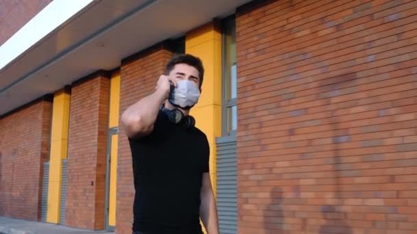 Jonge man met een masker luistert naar muziek en praat aan de telefoon — Stockvideo