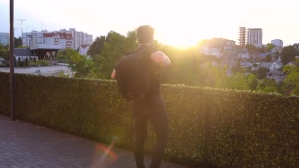 Cadre mobile derrière un touriste au coucher du soleil. Touriste avec un sac à dos qui admire la ville. — Video
