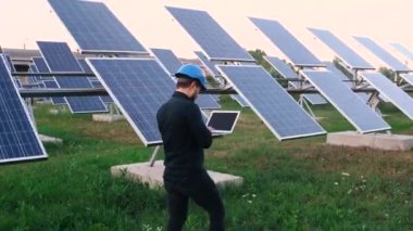 Kafkasyalı üniformalı sanayi mühendisi güneş panelleri arasında inceleme için yürüyor.