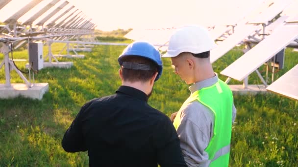 Молоді кавказькі чоловіки з інженерами сидять з планом будівництва на сонячній фермі. — стокове відео