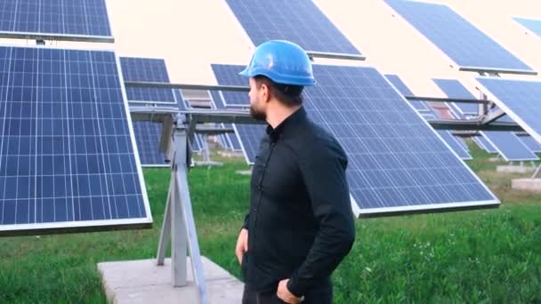 Un joven ingeniero sonríe en la habitación satisfecho con el trabajo en un fondo de panel solar. — Vídeo de stock