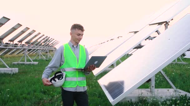 Engenheiro feliz, com equipamentos especiais, detém um laptop de onde ele controla a produtividade dos painéis solares. — Vídeo de Stock