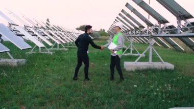 Bir mühendis ve bir iş adamının el sıkışarak birbirlerini selamladığı geniş bir çerçeve. Arka planda elektrik panelleri.