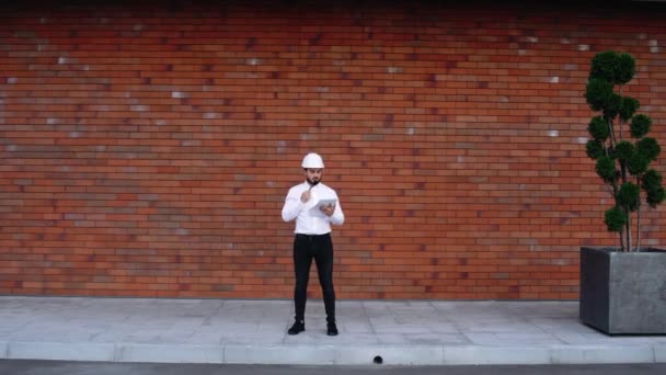 Breed frame voor een knappe blanke arbeider met een helm, buiten staand. — Stockvideo