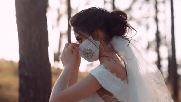 Un video de una novia en el parque. Se pone la máscara con ambas manos. La máscara es blanca. — Vídeos de Stock