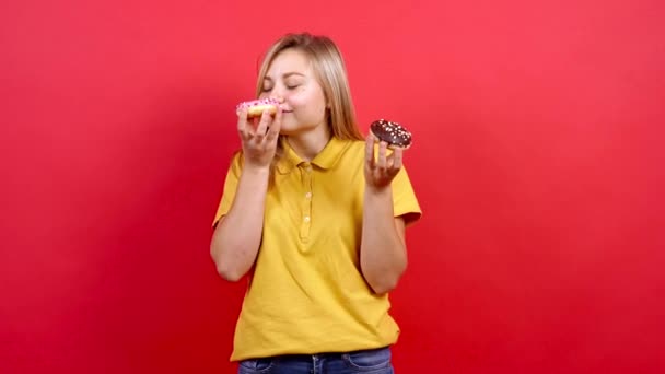 Menina bonita e gorda com uma camiseta amarela segurando dois donuts na mão. — Vídeo de Stock