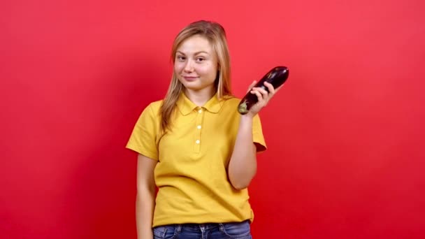 Schattig en licht dik meisje in een geel T-shirt met verse aubergines in haar hand, — Stockvideo