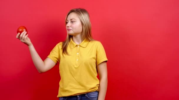 Linda y ligeramente gorda chica en una camiseta amarilla que sostiene un tomate fresco en su mano, — Vídeo de stock