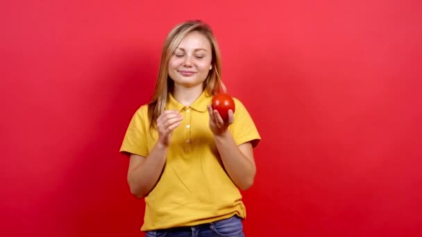 Linda y ligeramente gorda chica en una camiseta amarilla juega con un tomate fresco. — Vídeo de stock