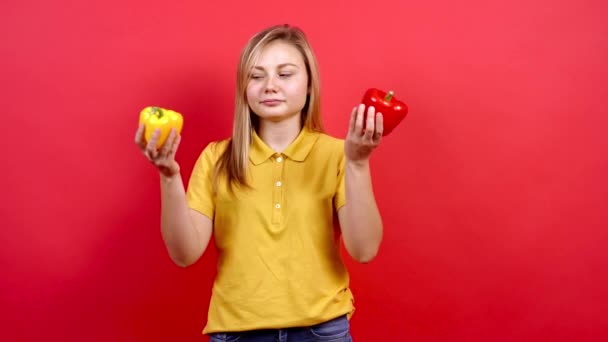 Menina bonito e ligeiramente gordo em uma camiseta amarela segurando uma pimenta amarela e vermelha em sua mão. — Vídeo de Stock