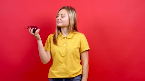 Schattig en licht dik meisje in een geel T-shirt houdt een rode ui in haar hand. — Stockvideo