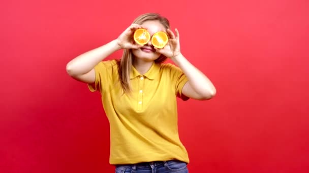 Счастливая, оптимистичная девушка в желтой футболке, закрывающая глаза мандаринами и показывающая свой язык, — стоковое видео