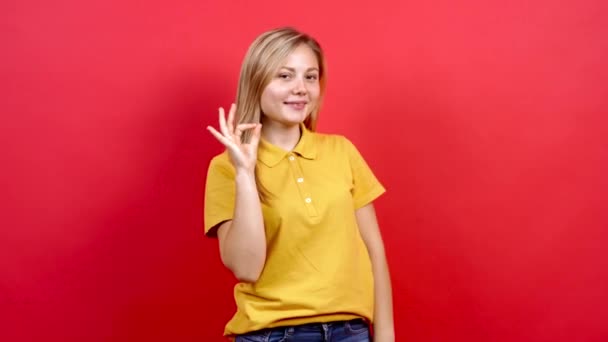 Vacker vit kvinna i gul T-shirt och lång blond hår, står på röd bakgrund, — Stockvideo