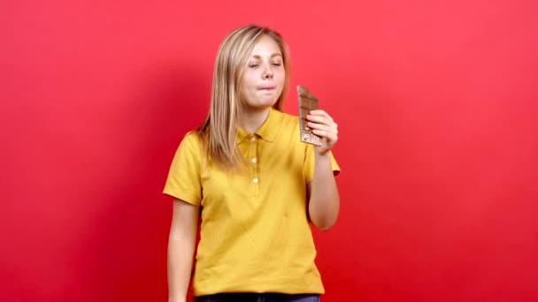 Schattig en een klein dik meisje in een geel T-shirt houdt een chocolade in haar hand. — Stockvideo