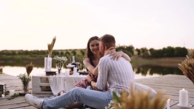 Genç aşıklar süslü ahşap bir güvertede otururken kucaklaşırlar..