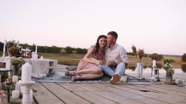 Coppia innamorata sono seduti su un ponte di legno sul lago. Ponte organizzato con decorazione per le richieste di matrimonio. — Video Stock