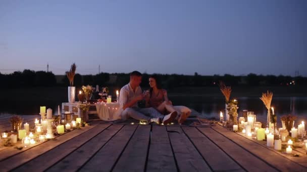 Романтическая пара. Молодые люди в любви пьют шампанское на палубе, украшенной свечами. — стоковое видео