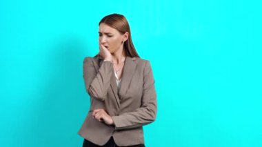 İş elbisesi giymiş hayal kırıklığına uğramış genç bir kadın, yanağına dokunuyor, keskin diş ağrısı çekiyor.