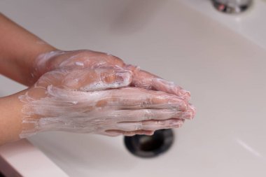 Banyo lavabosunun üzerinde köpükle ellerini yıkamak.