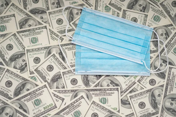 Two disposable blue masks on the background of hundred dollar bills. Business and finance