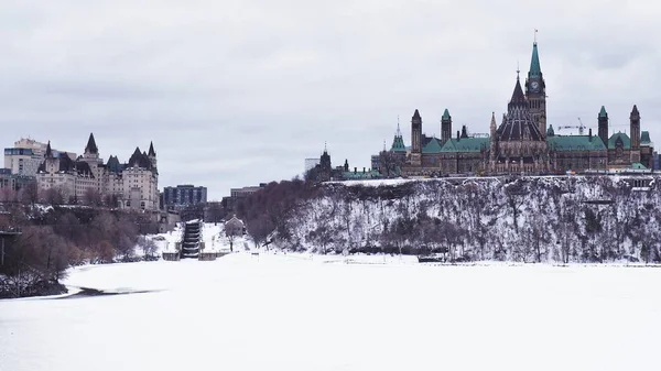 Landscape of Parliament Hill in Ottawa, Ontario, Canada.  The Parliament Building on Canada stands tall on Parliament Hill on a cold winter day, with the Ottawa River still frozen from the dog days of winter.