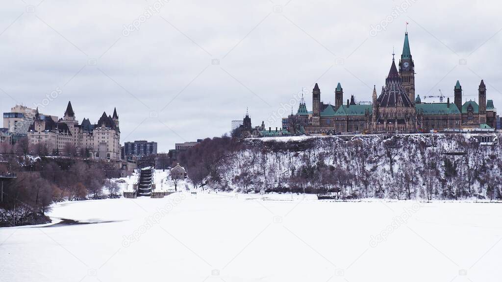 Landscape of Parliament Hill in Ottawa, Ontario, Canada.  The Parliament Building on Canada stands tall on Parliament Hill on a cold winter day, with the Ottawa River still frozen from the dog days of winter.