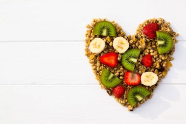 Kalbi tahıl gevreği ve beyaz ahşap bir arka planda meyveler gibi yatıyordu. Düz yatıyordu. Boşluğu kopyala.