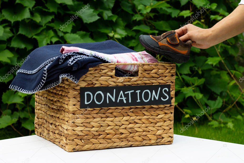 Hand putting a children shoes in a box for clothing donations on a greenery background. Charity and donation concept, copy space.