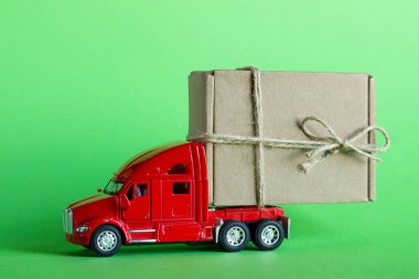Kırmızı oyuncak araba kamyonu yeşil arka planda bir karton kutuda bir paket teslim ediyor. Mal teslimatı, hediye ya da bağış konsepti.